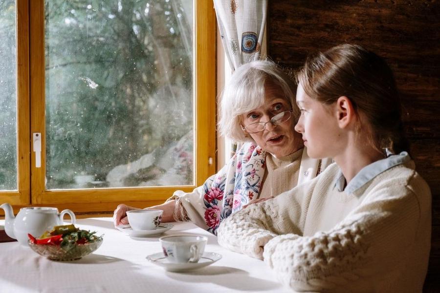 Ältere und jüngere Frau sitzen mit Tassen an einem Tisch und unterhalten sich