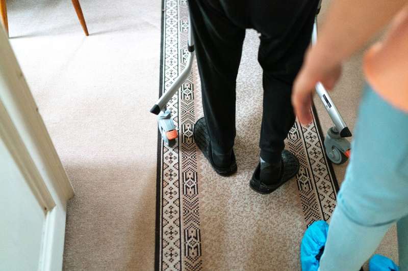 Gehhilfe und Füße einer älteren Person auf einem Teppich im Wohnbereich